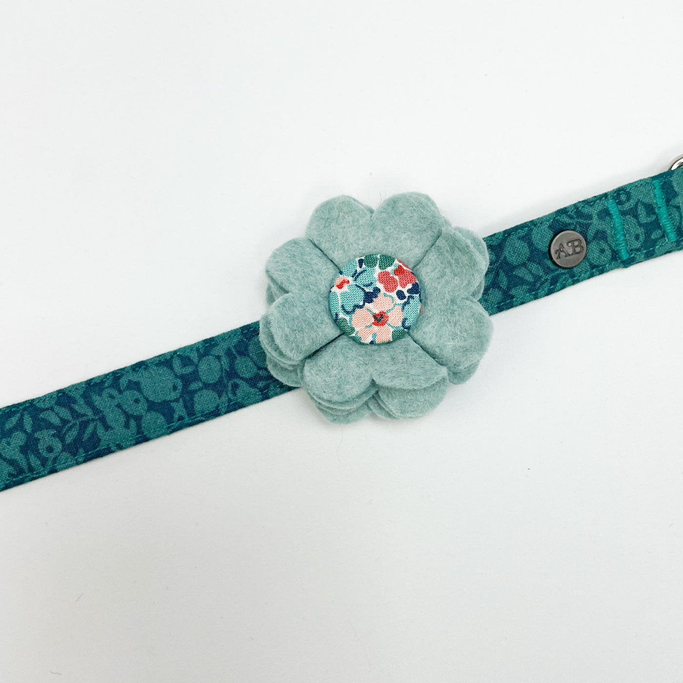Dog collar flower accessory in soft teal felt with a Liberty fabric button shown on a Liberty Winter Floral collar.