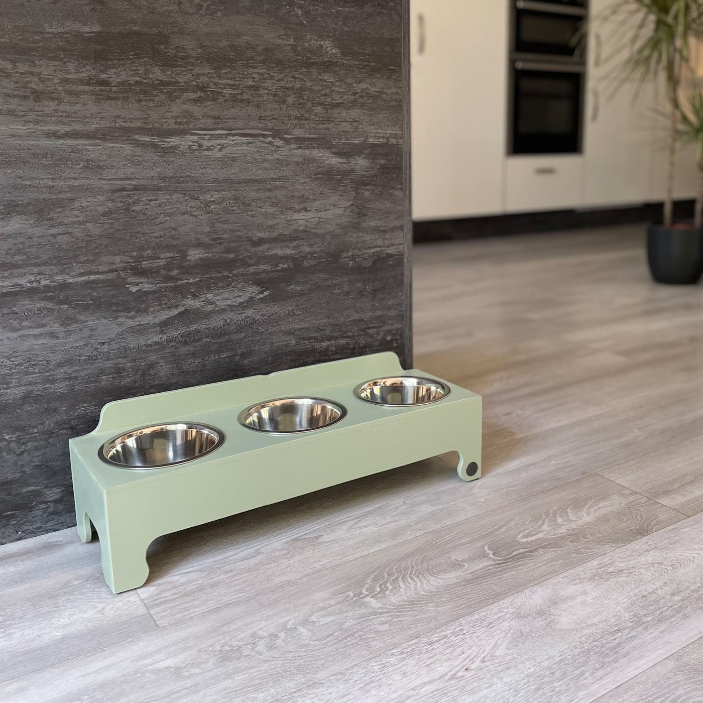 Medium raised triple-bowl dog feeding stand in soft green.