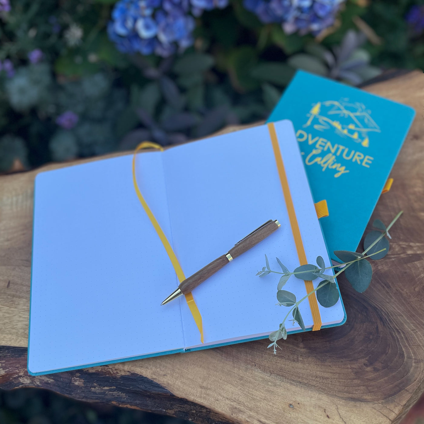 Bright blue hardback notebook with Yellow pen loop, elastic and bookmark, "Adventure is calling" embossed on the cover.
