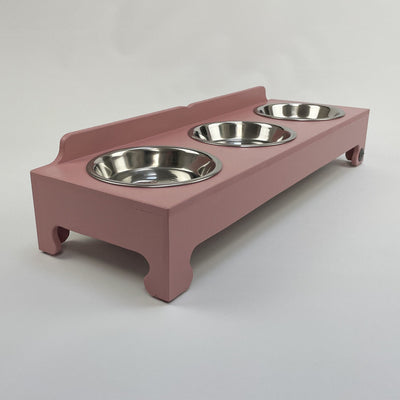 Cat/puppy raised bowl feeding stand in blush pink with three stainless steel shallow food dishes.
